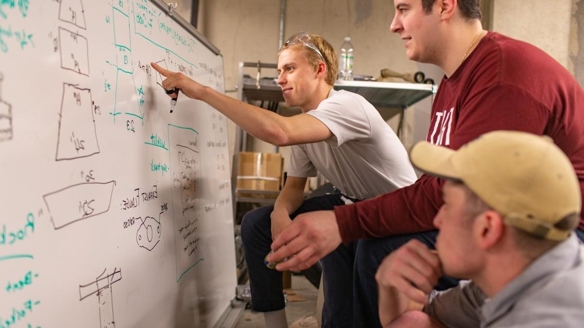 Students writing on a whiteboard discussing a project